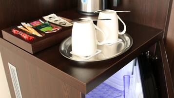 A hotel room with a wooden desk, a tray with cups and a kettle, and a laptop on a stand.
