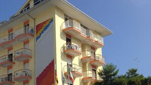 A multi-story building with balconies, a staircase, and flags. - Hotel MaxiHeron (Jesolo)