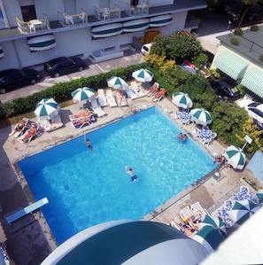 A rooftop pool with clear blue water, surrounded by lounge chairs and umbrellas, and a view of the cityscape in the background. - Hotel MaxiHeron (Jesolo)