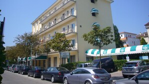 Um hotel com vários andares, varandas, estacionamento e uma árvore verde à frente.