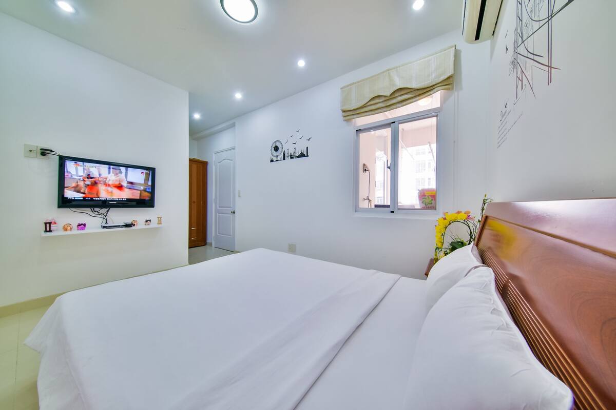 Une chambre d’hôtel avec un lit, un téléviseur fixé au mur, une fenêtre avec un rideau et un élément décoratif sur le mur.