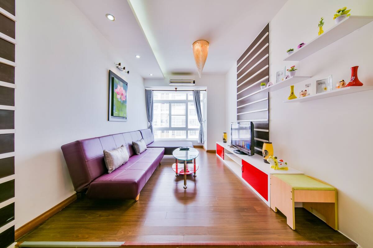 Un salon moderne comprenant un canapé, une petite table ronde, un téléviseur et des étagères ornées d’objets décoratifs.