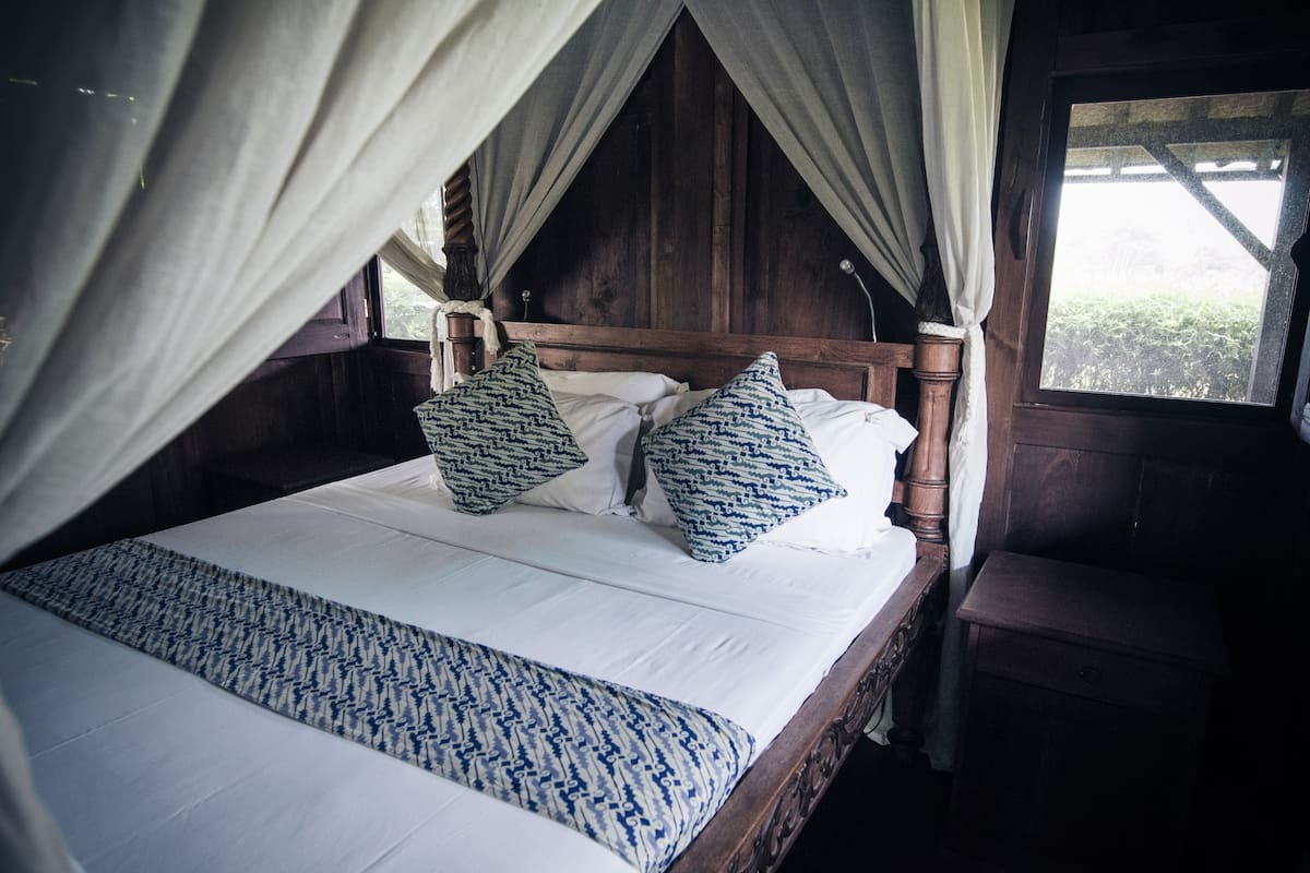 Una cama con dosel, cabecera de madera y almohadas estampadas.