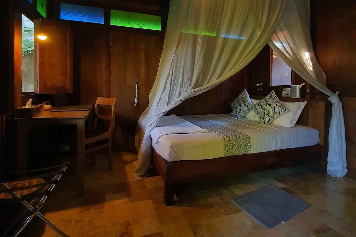 Una habitación con cama bajo un dosel, un escritorio con silla y una alfombra pequeña en el suelo.