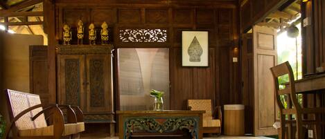 A room with a wooden ceiling, a cabinet with decorative items, a table with a vase, and a chair.