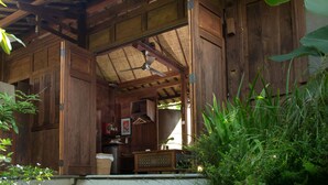A rustic wooden structure with a ceiling fan, wooden walls, and a small kitchen area visible through an open door. - Yabbiekayu Eco Bungalows (Sewon)