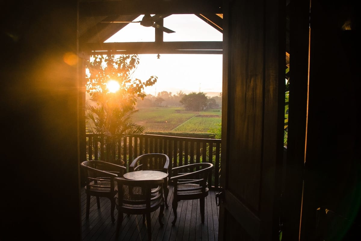 Una terraza de madera con una mesa y sillas, con vistas a un paisaje rural con campos y una puesta de sol.