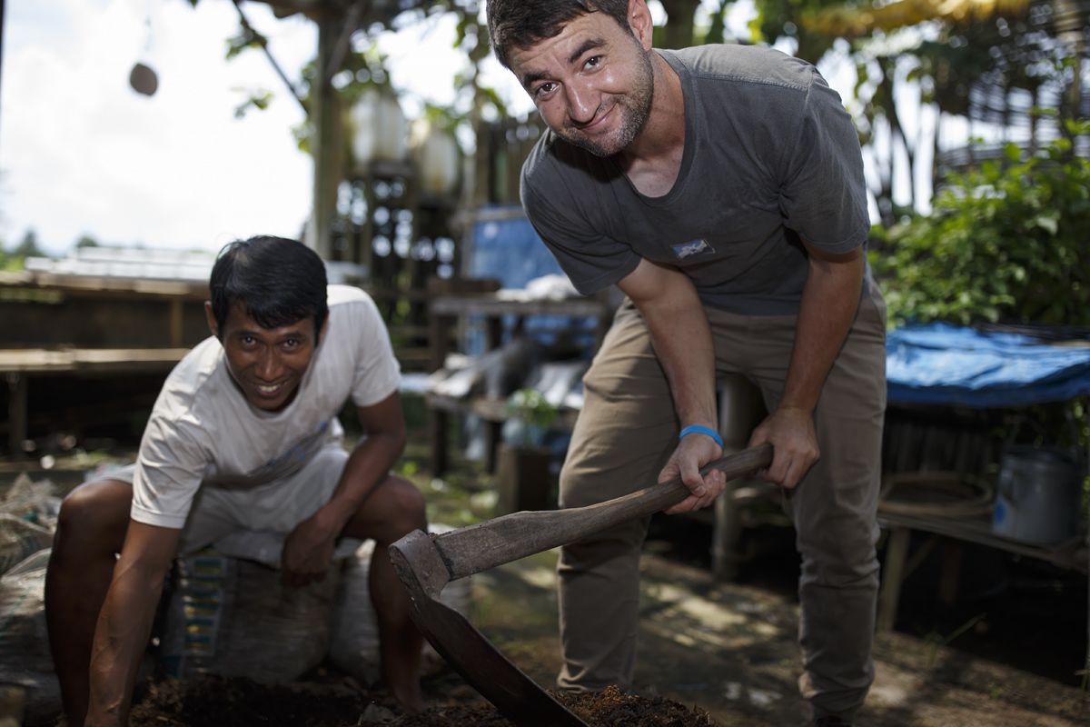Two individuals working outdoors, one using a shovel.