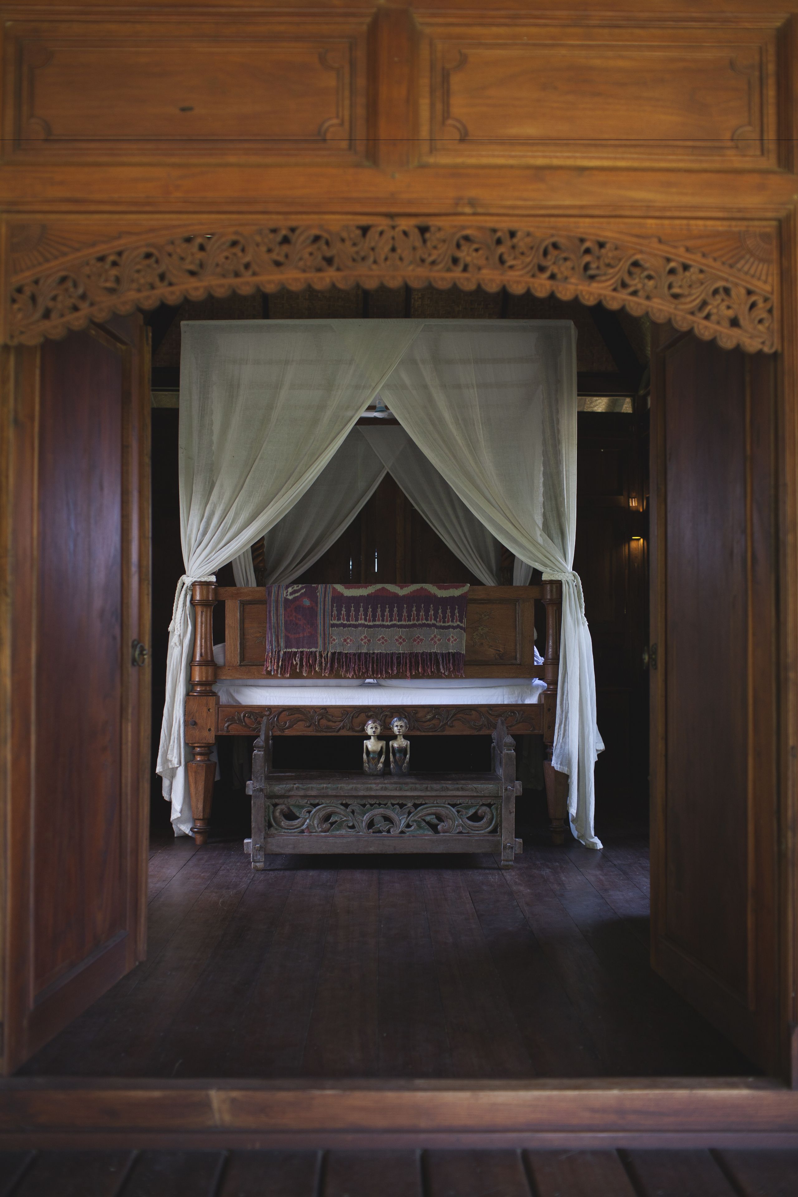 Una cama de madera con dosel, una mesita de noche y un espejo decorativo.