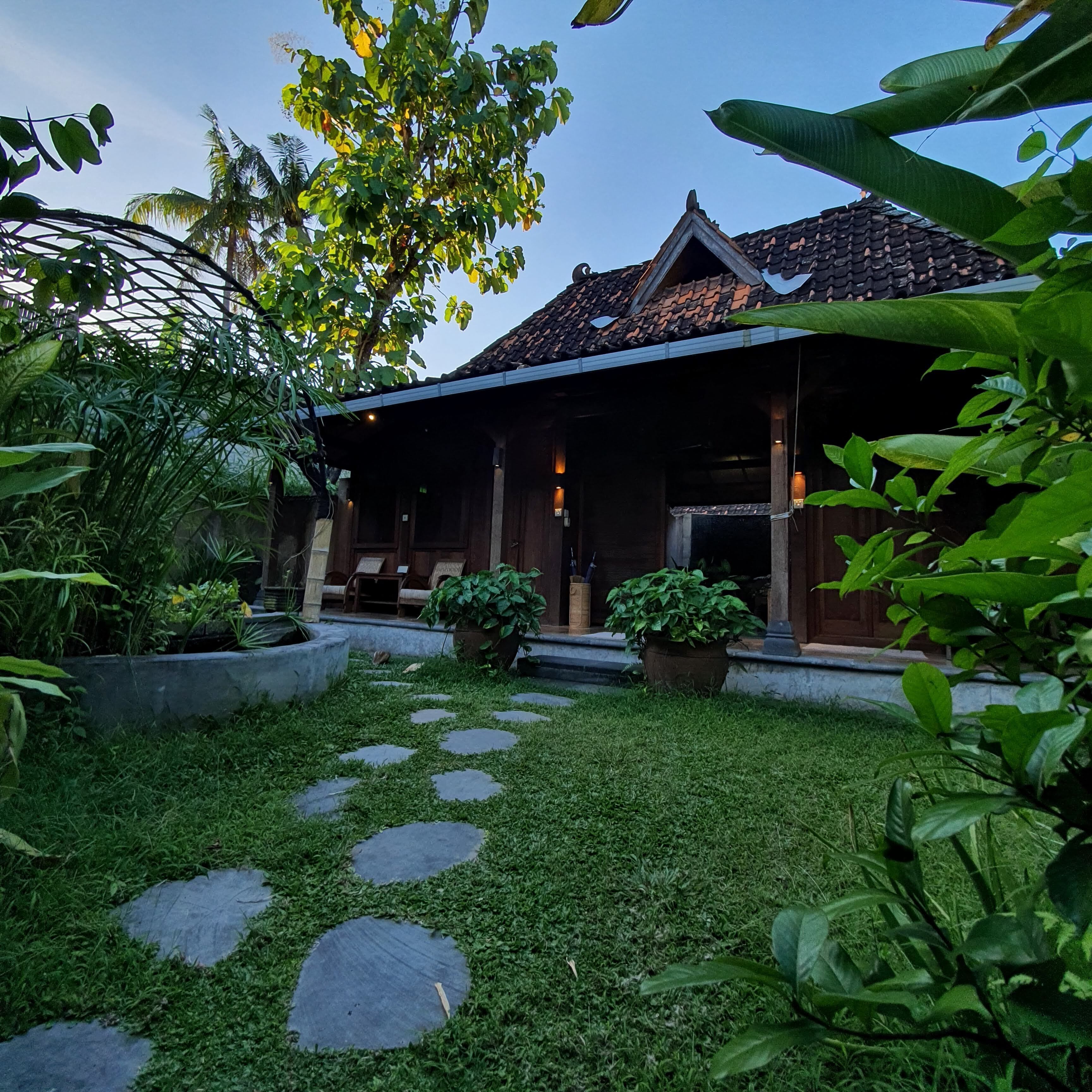 A traditional house with a tiled roof, a covered porch with seating, and a garden with stepping stones and potted plants.