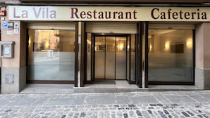 De ingang van Restaurant Cafeteria La Vila, met een glazen deur en een bord erboven.