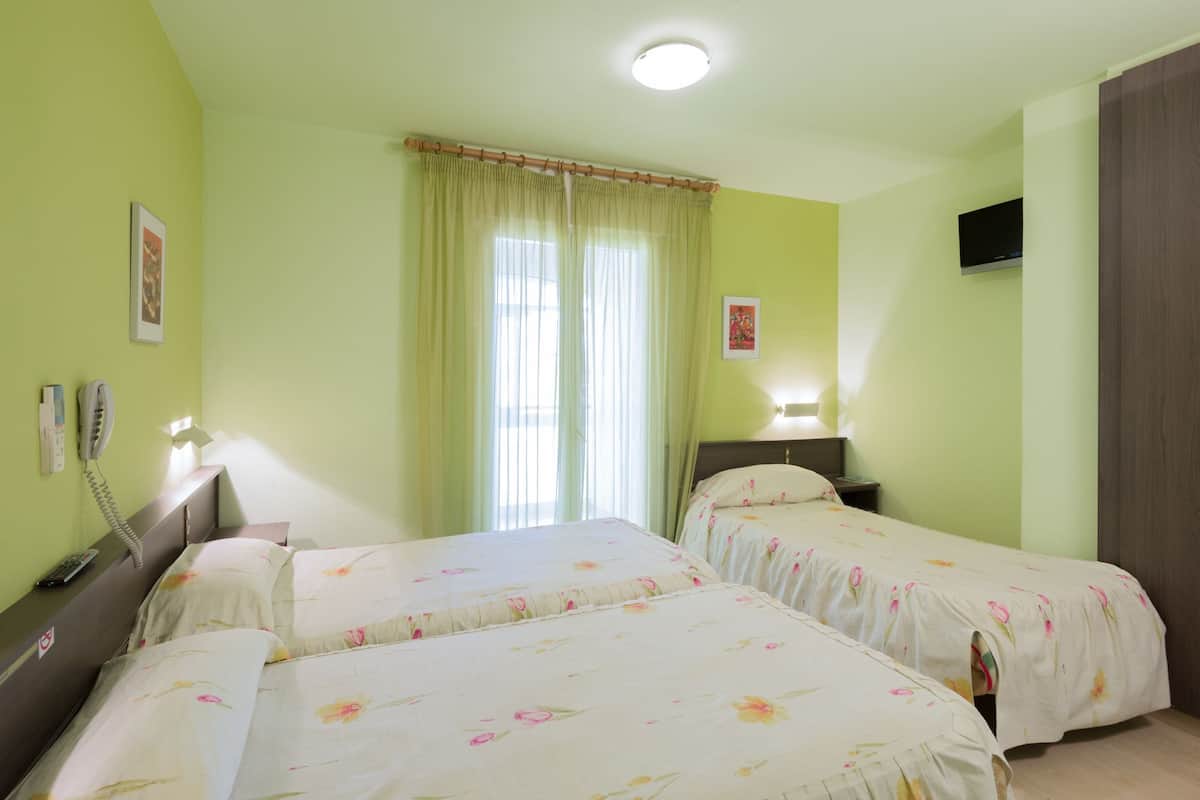 Una habitació d'hotel amb dos llits, una taula de nit amb una làmpada, un telèfon i un televisor fixat a la paret.