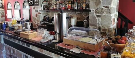 A breakfast buffet with a variety of food items, a coffee station, and a selection of beverages on a stone wall backdrop.