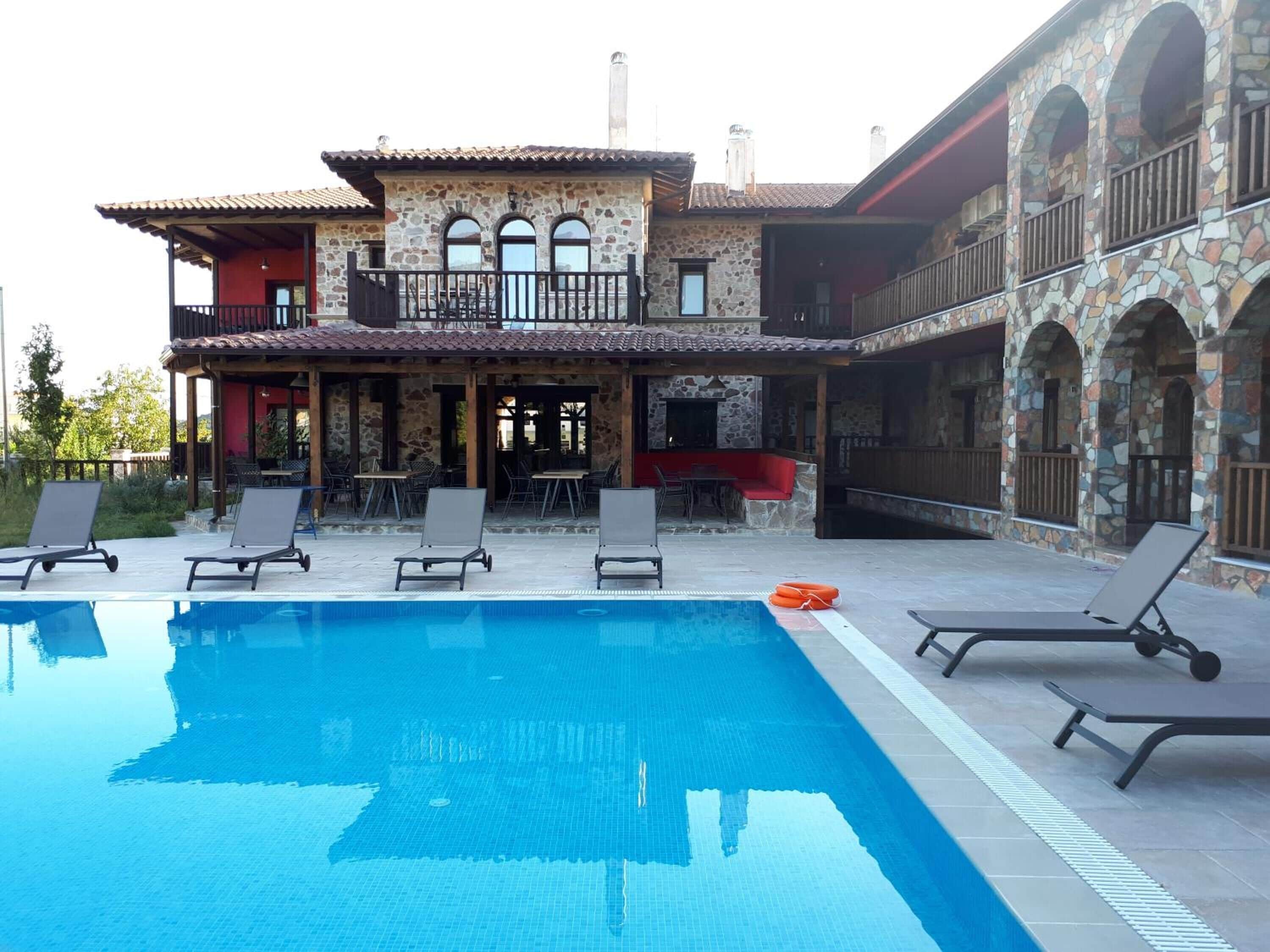 Ein zweistöckiges Steinhaus mit Schwimmbad, Außenbereich zum Sitzen und einer überdachten Terrasse.