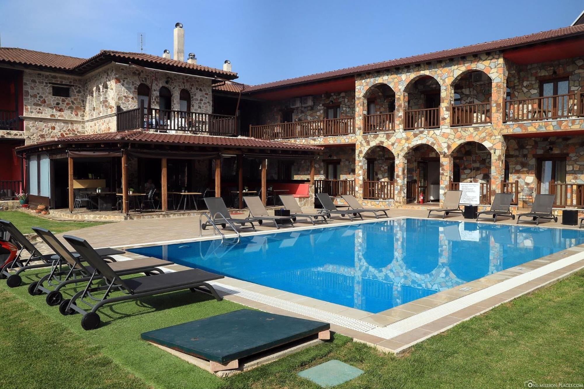 Un área de piscina con sillones de descanso y un edificio de piedra con arcos.