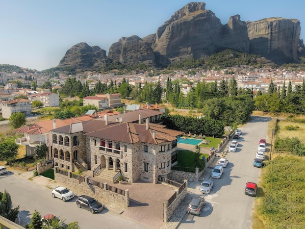 A stone building with a red-tiled roof, a swimming pool, and a parking area with several cars.
