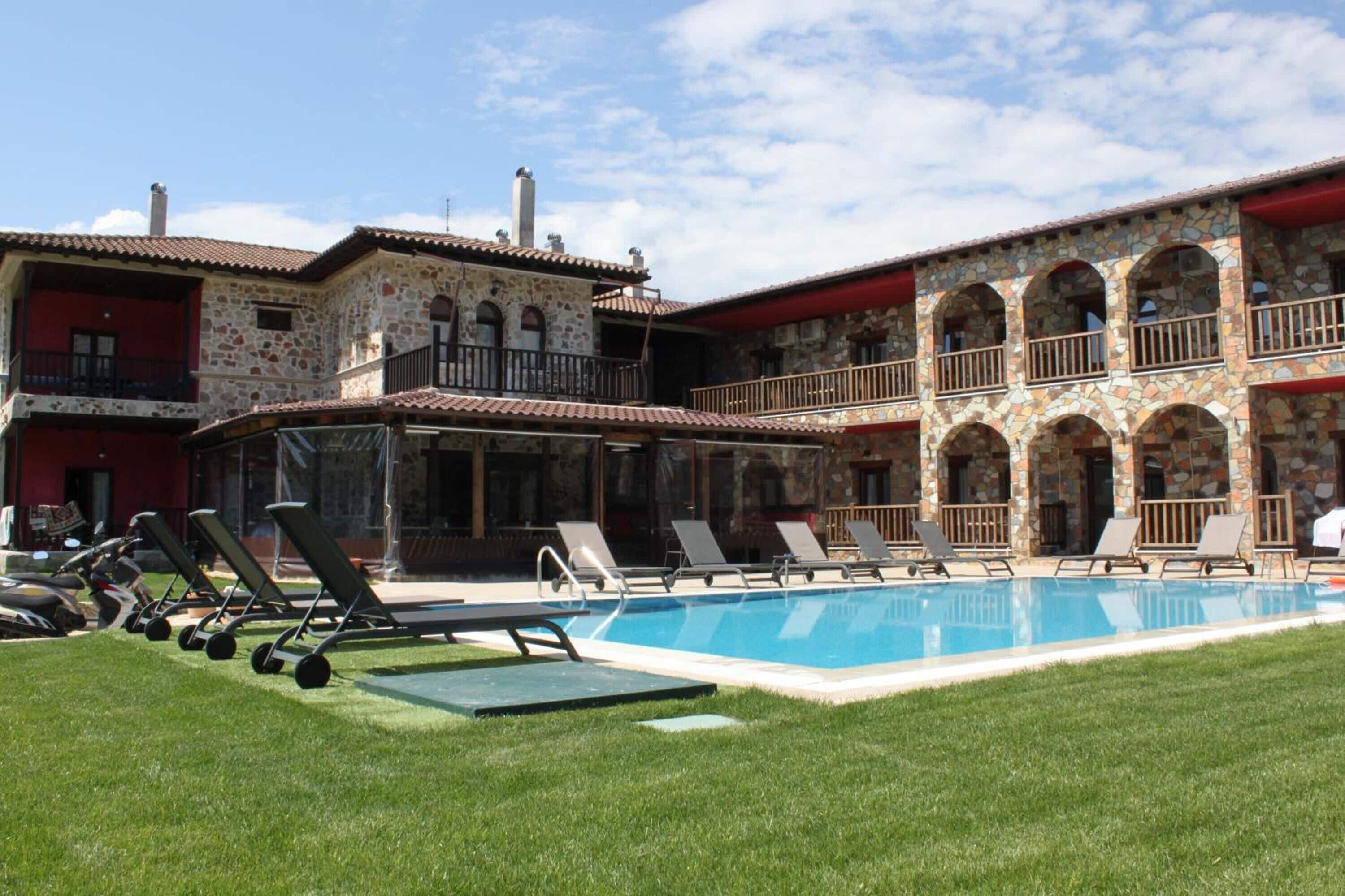 Zona de piscina con sillones de descanso y un edificio de piedra con balcones.