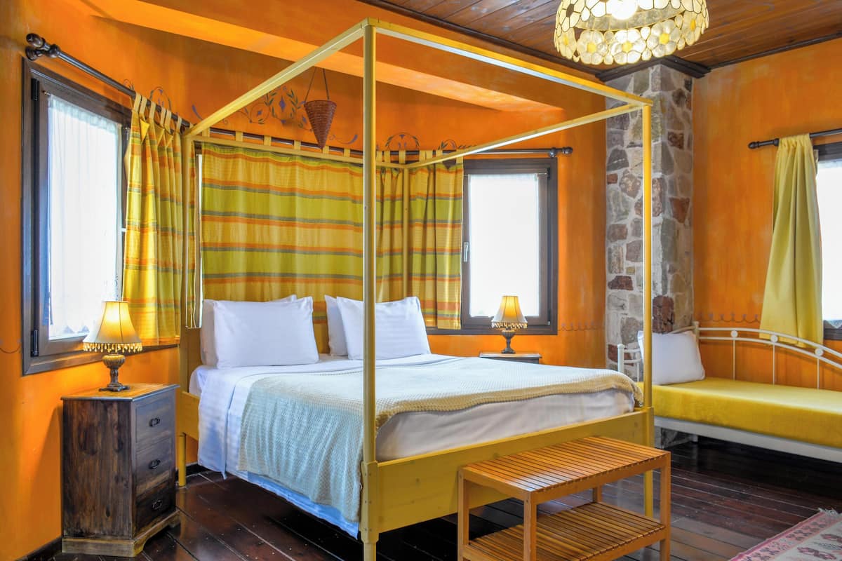 A room with a four-poster bed, a wooden nightstand, a bench, and a stone wall.