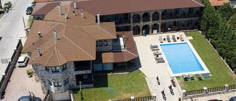 Un edificio grande con piscina, fachada de piedra y varias chimeneas.