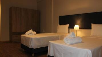 Een hotelkamer met twee bedden, elk voorzien van witte lakens en handdoeken, een houten garderobe en een bedlampje.