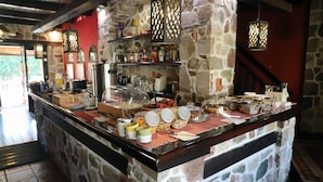 A breakfast bar with a stone wall backdrop, a coffee station, and hanging lanterns. - Guesthouse Monastiri (Kalabaka)