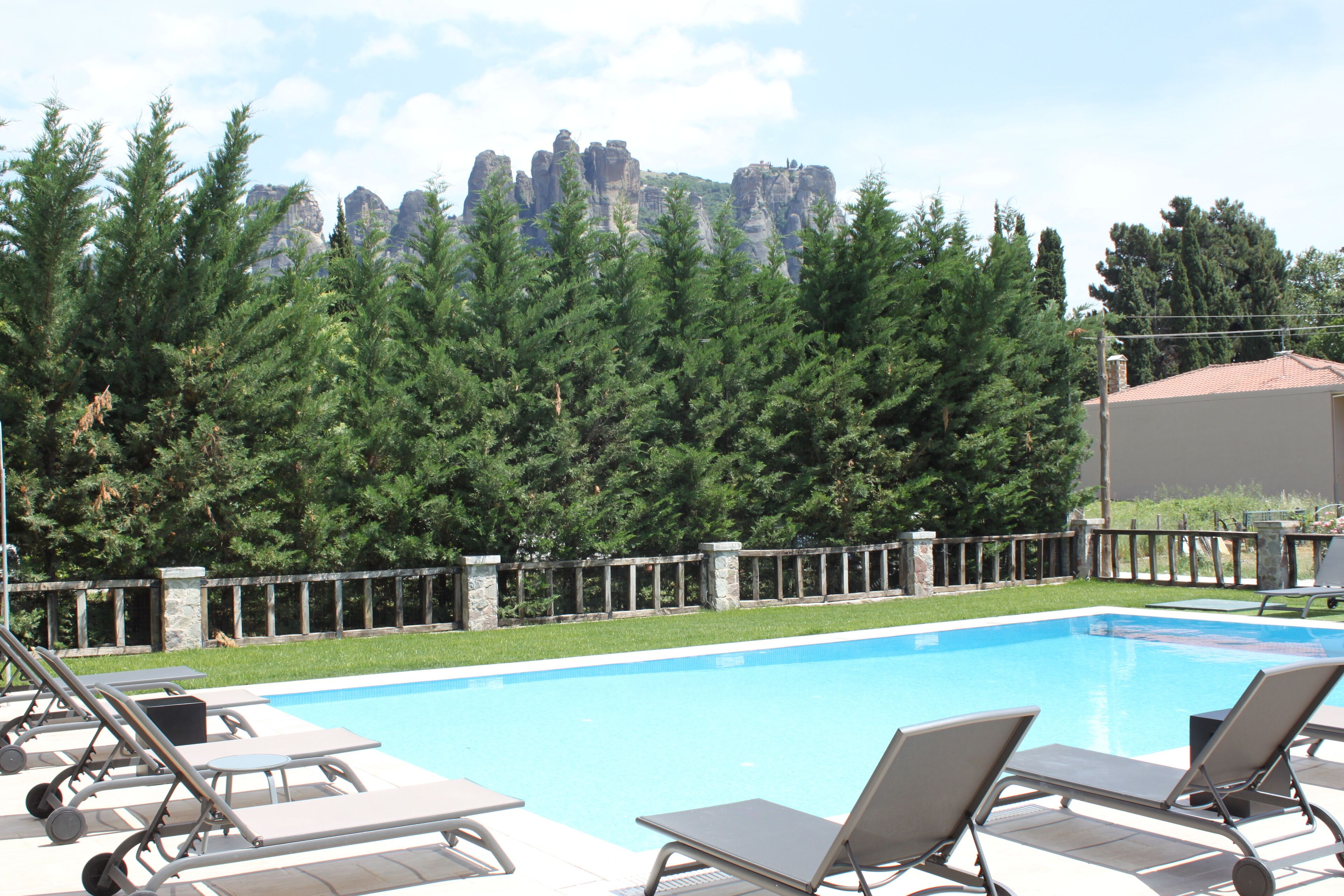 Ein Schwimmbecken mit Liegestühlen, umgeben von einer Steinmauer und Bäumen, mit Blick auf die Berge im Hintergrund.