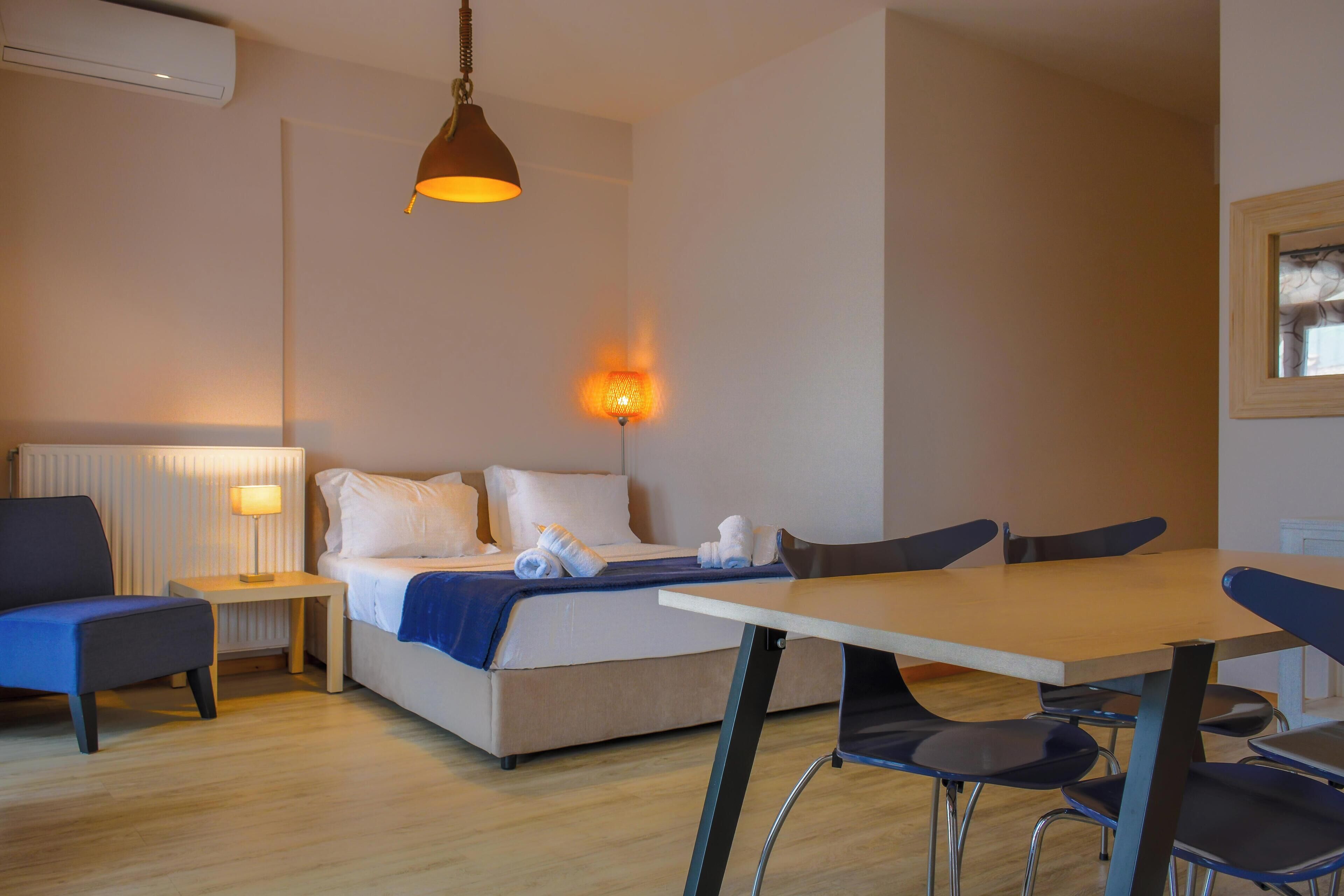A hotel room with a bed, a table, chairs, a lamp, and a wall-mounted light.