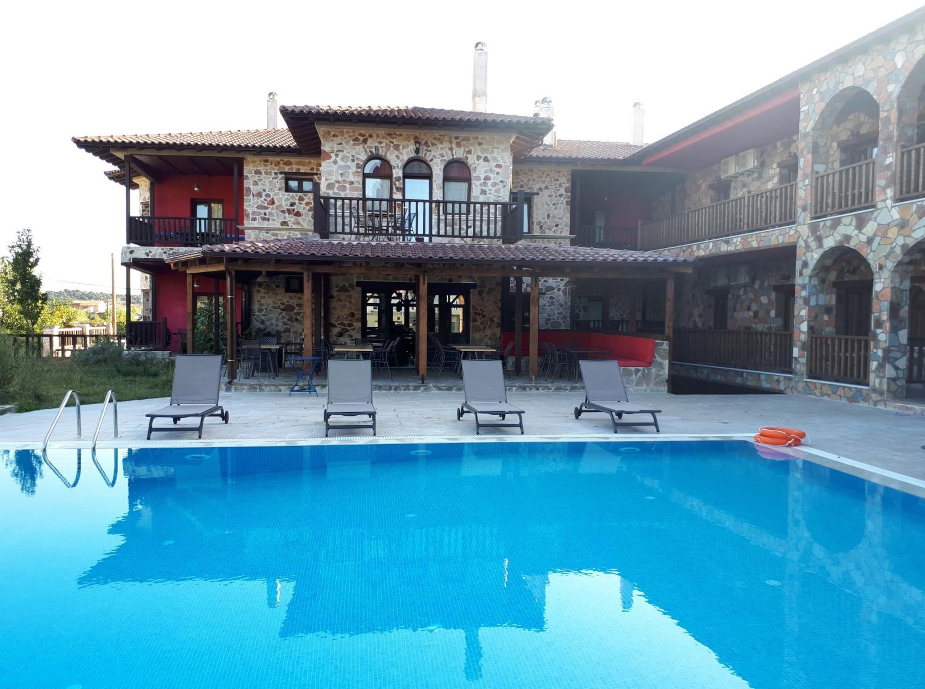 A two-story stone building with a swimming pool, outdoor seating, and a covered patio area.