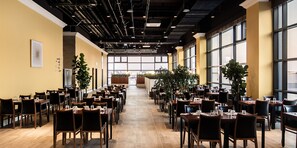 A spacious indoor dining area with multiple tables and chairs, large windows on one side, and a high ceiling with exposed pipes. - WesternLife Hotel (Iksan)