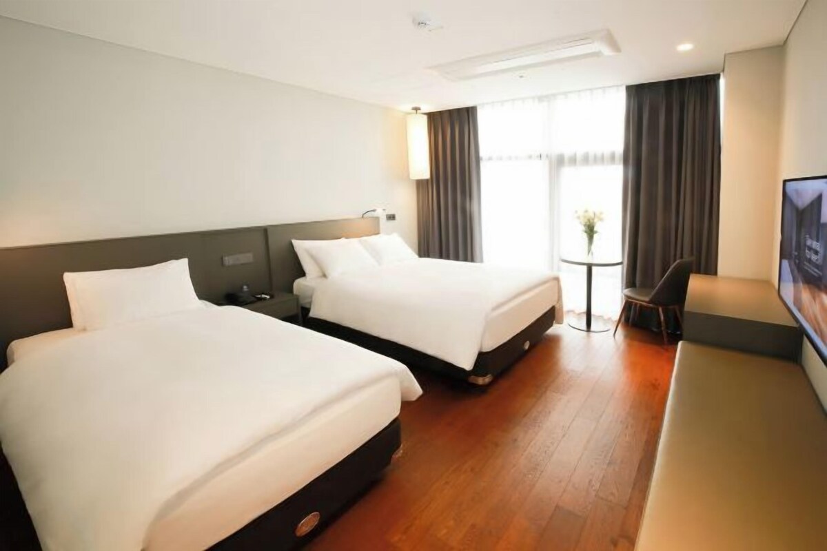 A hotel room with two beds, a desk, a chair, and a TV.