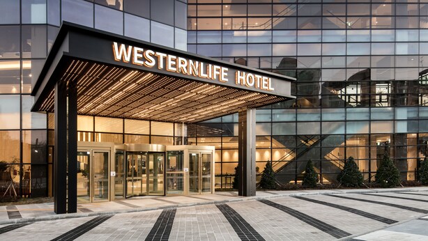 De ingang van Hotel Western Life met een moderne glazen gevel, een draaideur en een overdekt inkomgedeelte.