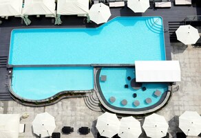 A rooftop swimming pool with a curved edge, surrounded by lounge chairs and umbrellas.