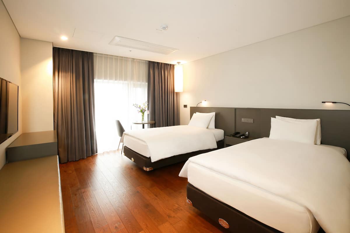 Ein Hotelzimmer mit zwei Betten, einem Schreibtisch, einem Stuhl, einer Lampe und einem fenster mit Vorhängen.