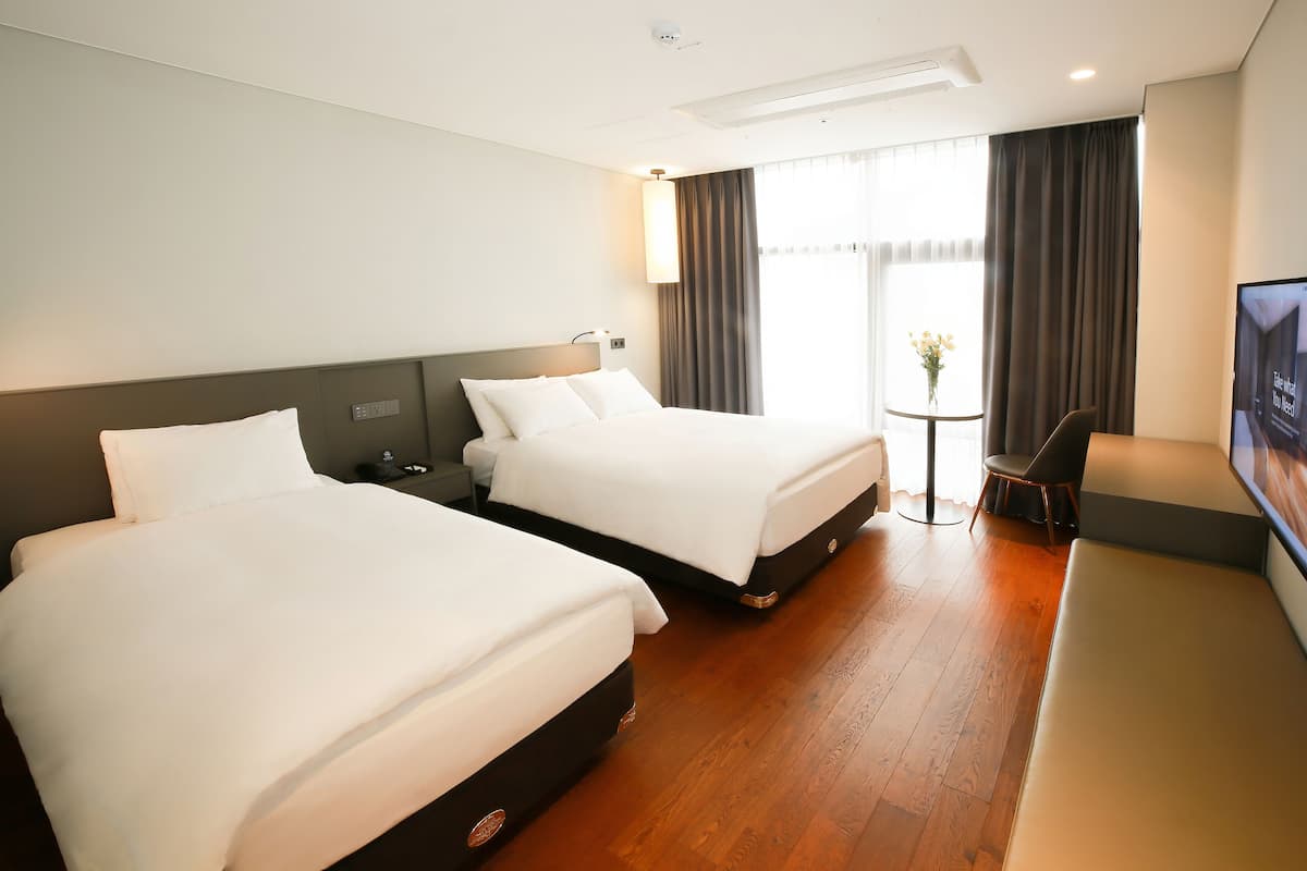 Ein Hotelzimmer mit zwei Betten, einem Schreibtisch, einem Sessel und einem Fernseher.
