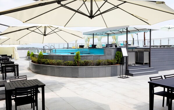 A rooftop pool area with multiple umbrellas, seating arrangements, and a bar counter. - WesternLife Hotel (Iksan)