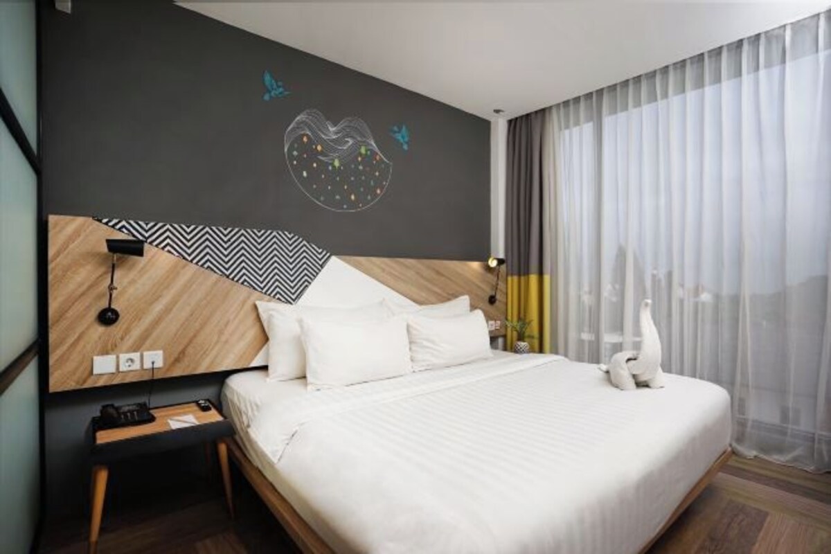Una habitación de hotel moderna con una cama grande, cabecera de madera, una lámpara de pared y una pieza de arte decorativo.