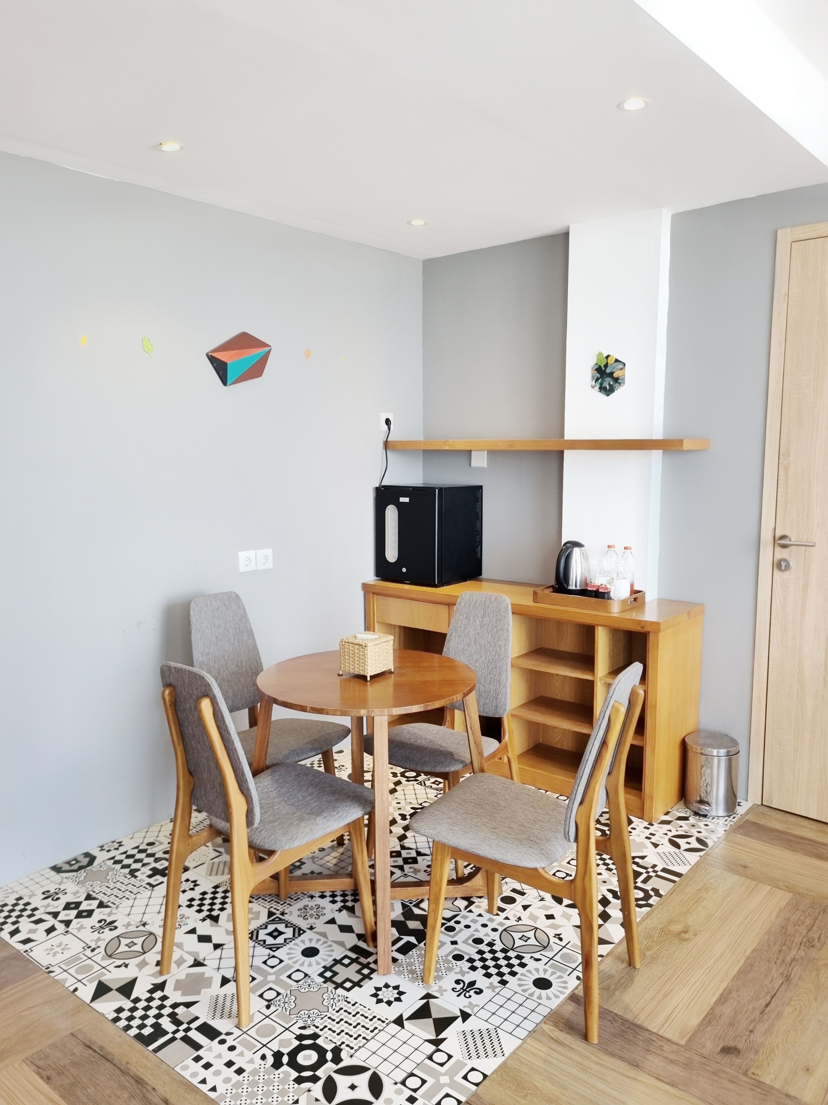 Un petit coin repas avec une table ronde, quatre chaises, un réfrigérateur noir et une étagère en bois où sont rangés des ustensiles de cuisine.