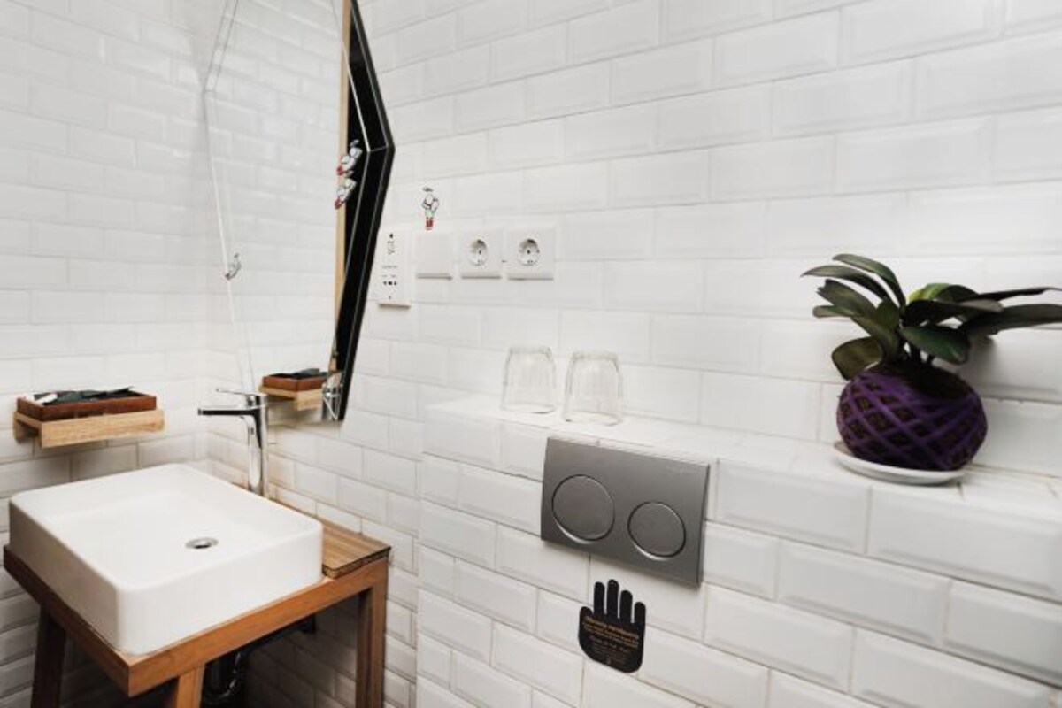 Un baño moderno con pared de azulejos blancos, tocador de madera, lavabo grande, espejo y grifo empotrado.