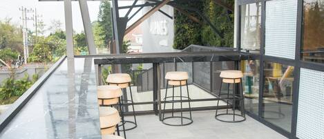 Un área de estar moderna al aire libre con taburetes de bar y barandilla de cristal con vistas a la ciudad.