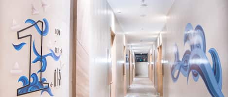 A hotel hallway with a long corridor, doors on both sides, and artistic wall decorations.