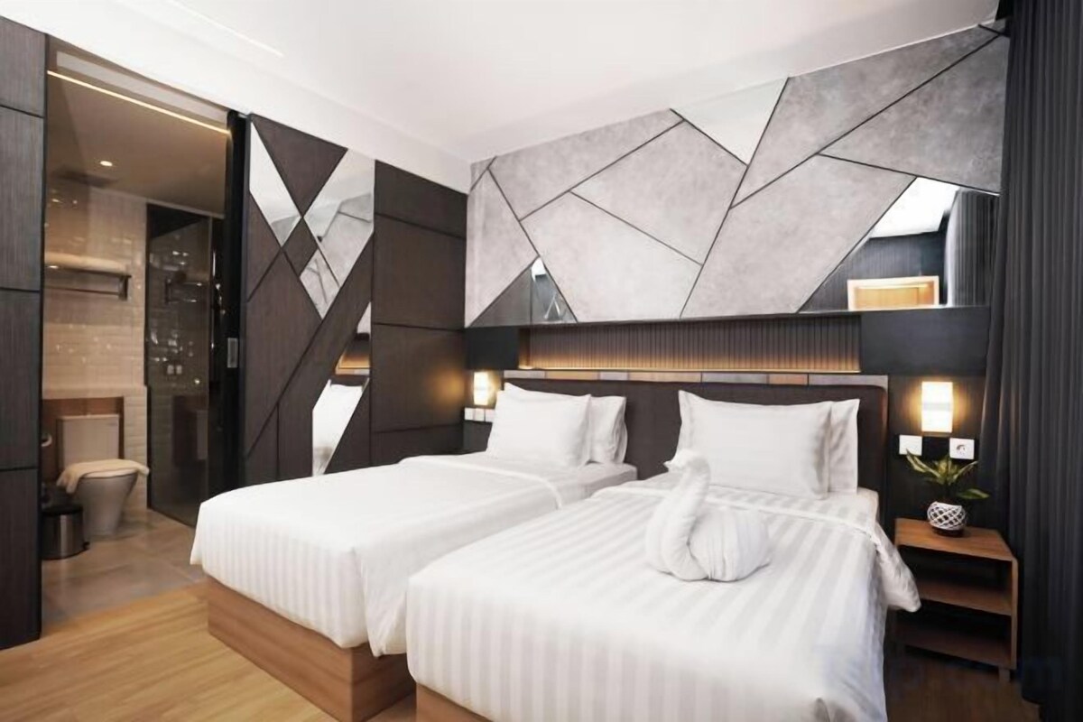 A modern hotel room with two beds, a large geometric wall design, and a small bedside table with a lamp.
