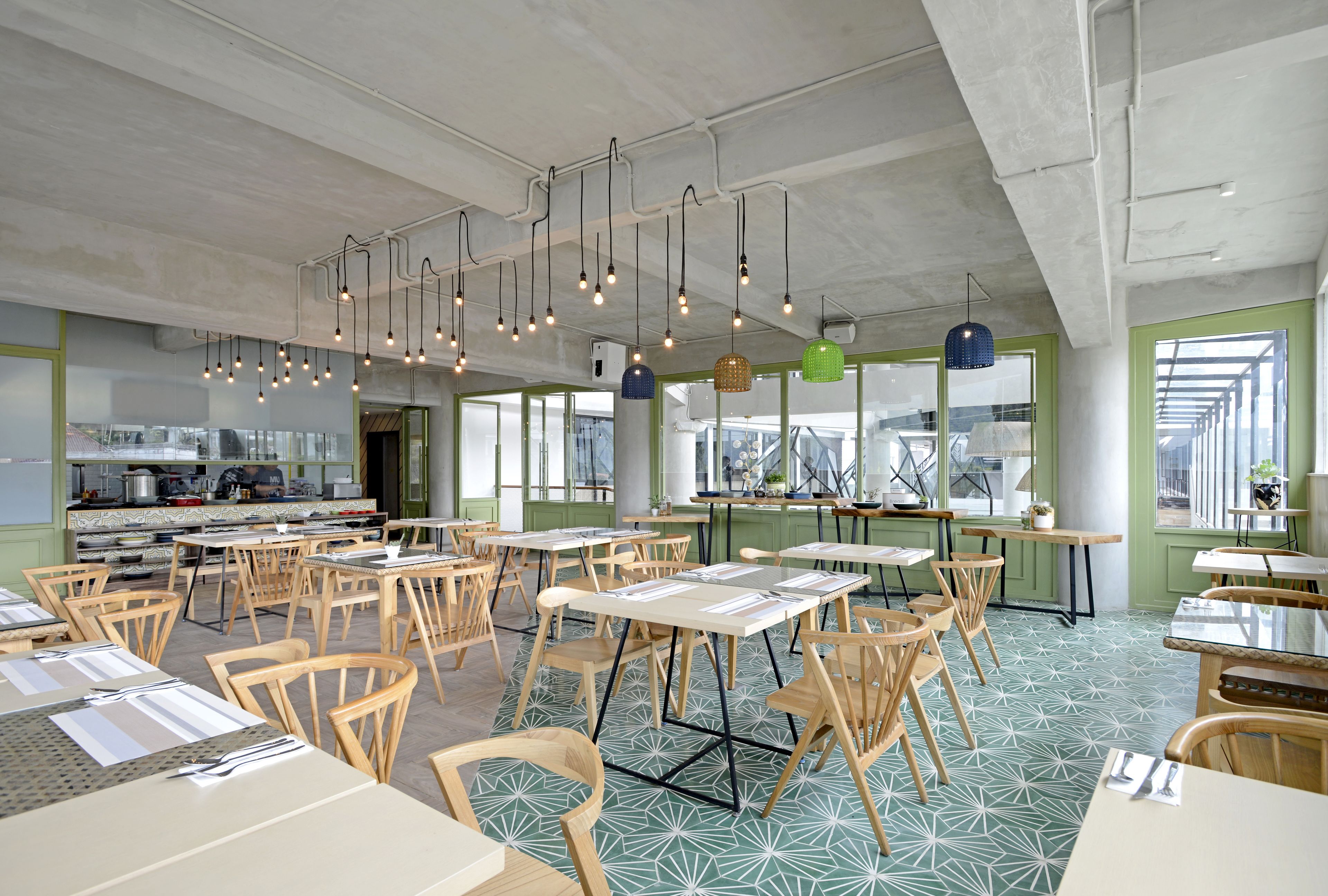 A spacious dining area with multiple tables and chairs, a kitchen in the background, and hanging pendant lights.