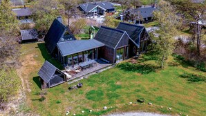 A modern house with a large deck, a covered outdoor area, and a well-maintained lawn. - 2 bedroom beach front home in Ebeltoft (Ebeltoft)