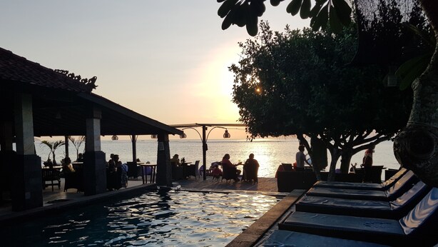 A poolside area with lounge chairs and a covered seating area overlooking the sea during sunset. - Puri Nusa Beach Hotel (Lembongan Island)