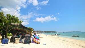 A beachside restaurant with outdoor seating, a sign reading "Puri Nusa," and a view of the sea and boats. - Puri Nusa Beach Hotel (Lembongan Island)