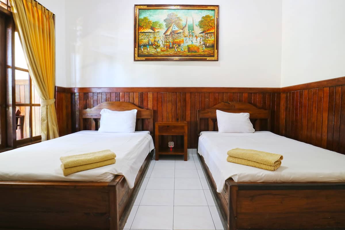 Una habitación de hotel con dos camas de madera, ropa de cama blanca, una mesita de noche de madera y un cuadro en la pared.