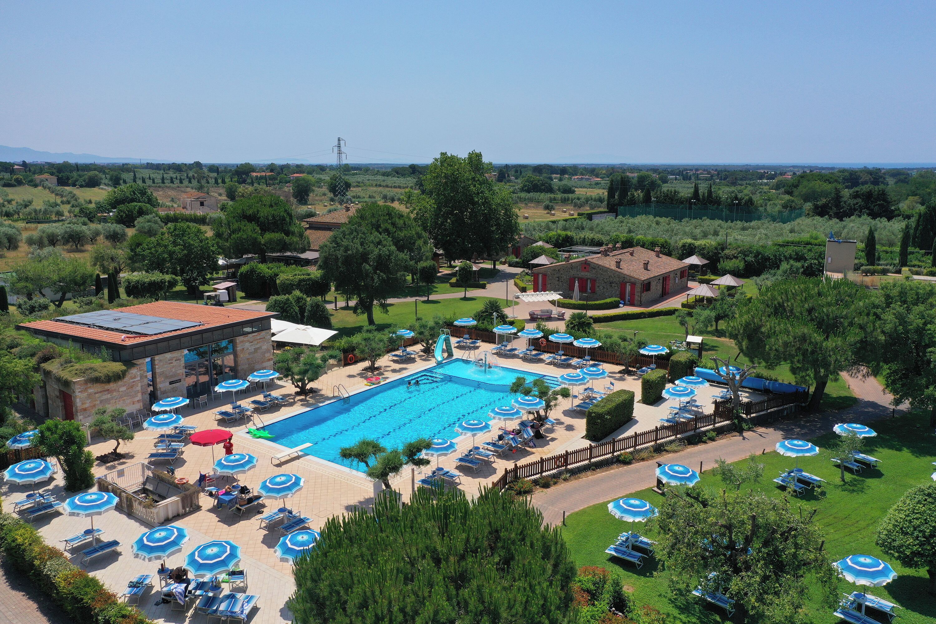 A swimming pool with lounge chairs and umbrellas, surrounded by greenery and a clear sky.