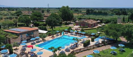 A swimming pool with lounge chairs and umbrellas, surrounded by greenery and a clear sky.