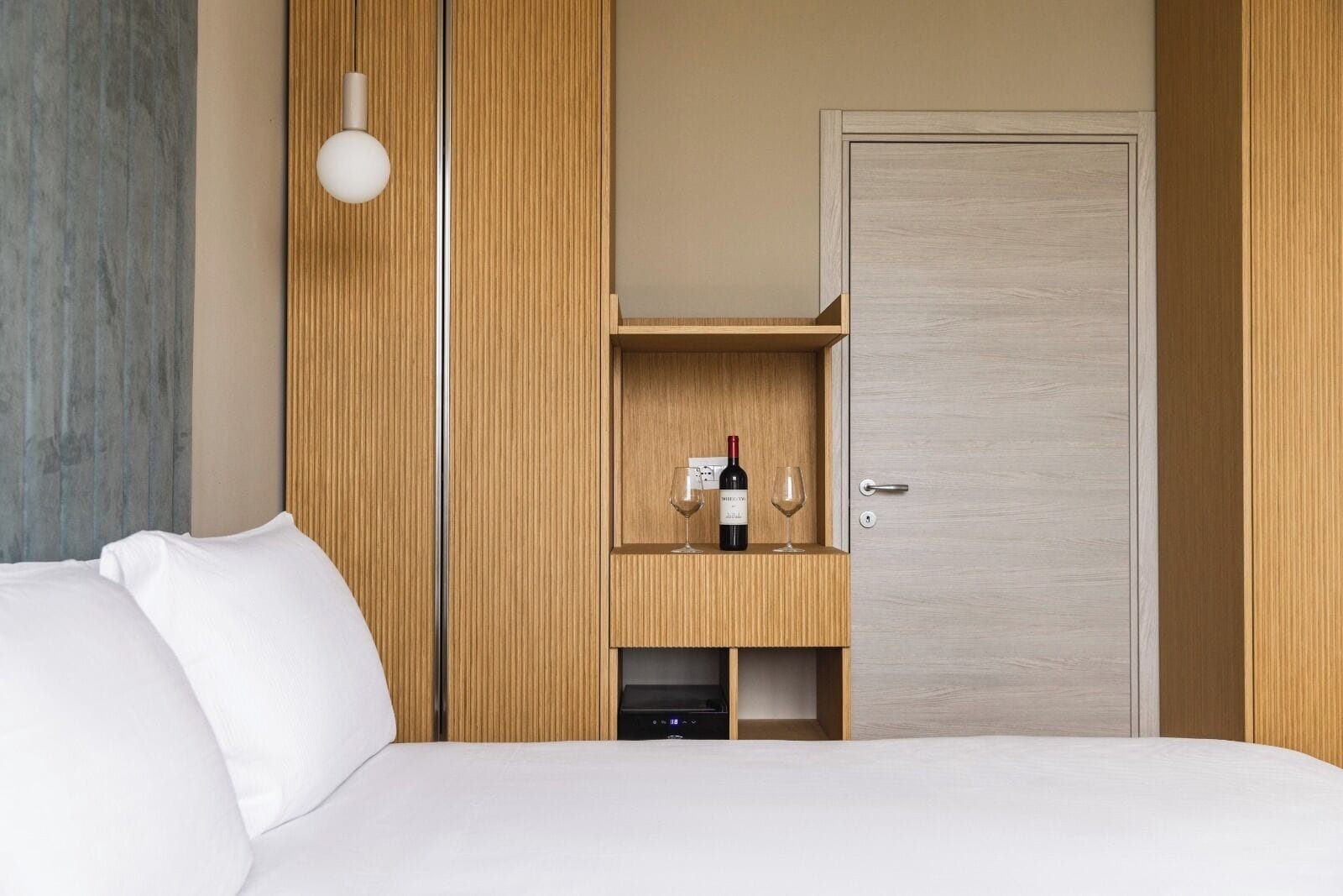 Habitación de hotel con cama, armario de madera, minibar y puerta.