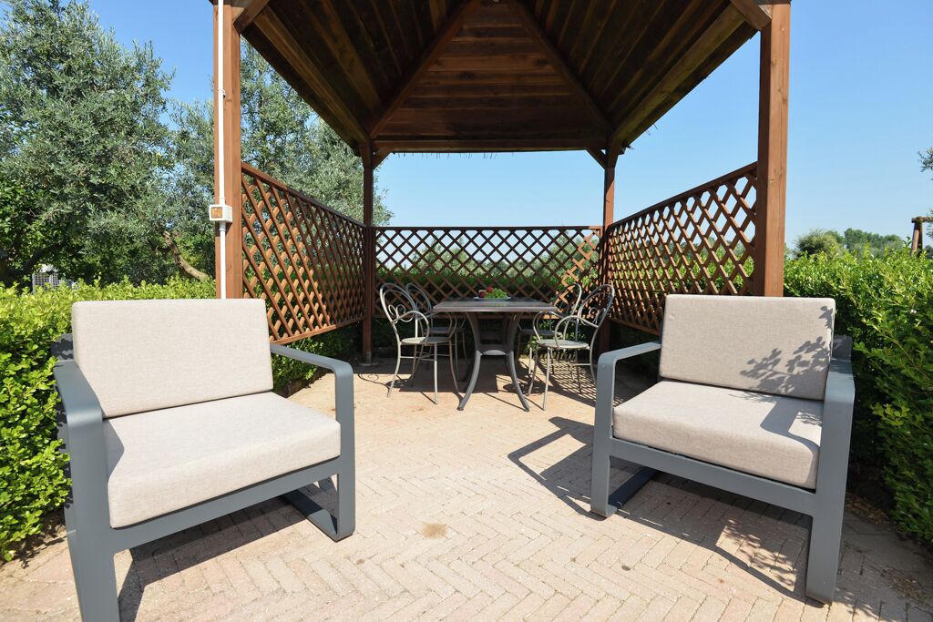 A covered outdoor seating area with two chairs and a table, surrounded by a wooden pergola and lattice fence.